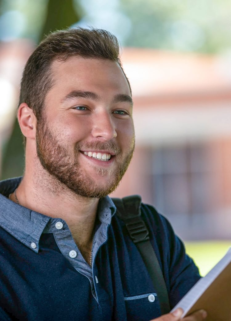 a male student looks through a notebook outside