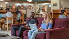 two students laugh while looking at a computer together