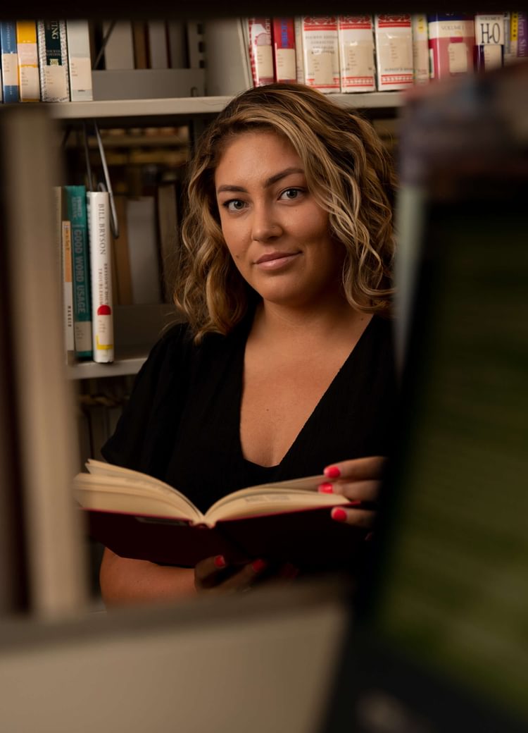 a female student looks at the camera through a shelf of books in the library