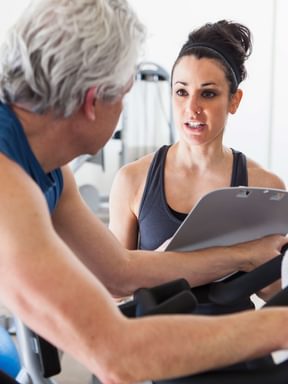 a fitness trainer works with a middle-aged man on an exercise bike