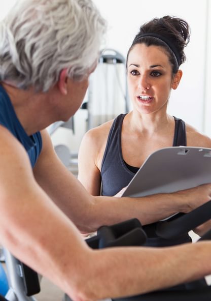 a fitness trainer works with a middle-aged man on an exercise bike