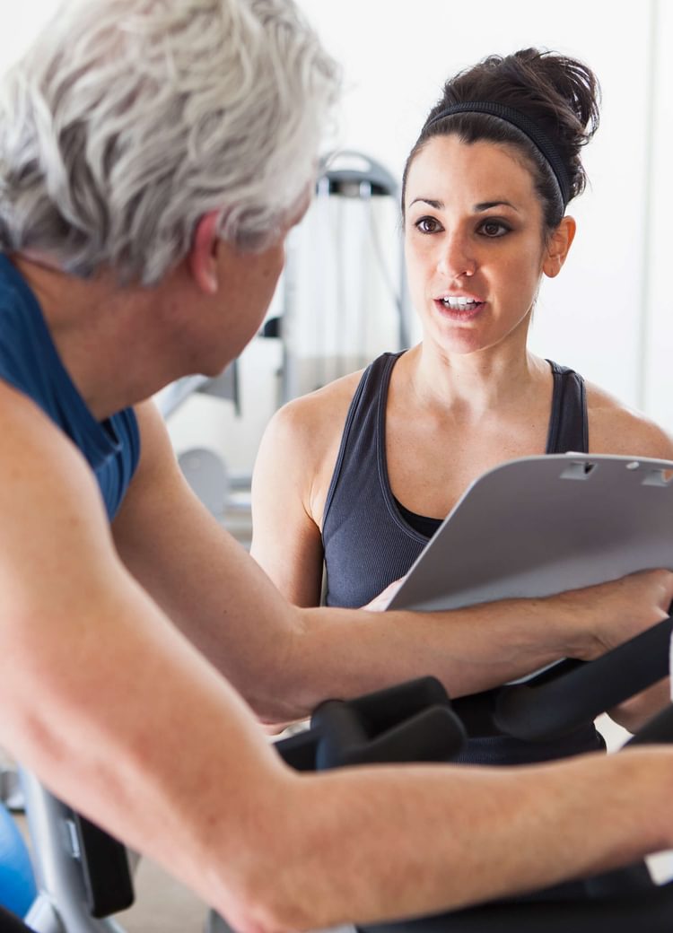 a fitness trainer works with a middle-aged man on an exercise bike