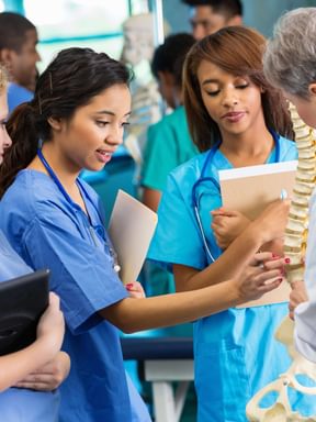 a group of nursing students discuss a skeletal model