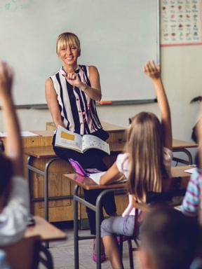 a teacher gets ready to call on a class of children with raised hands