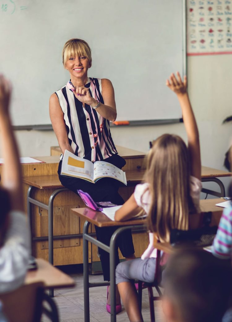 a teacher gets ready to call on a class of children with raised hands