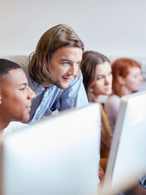 a professor stops to help students working on their computers