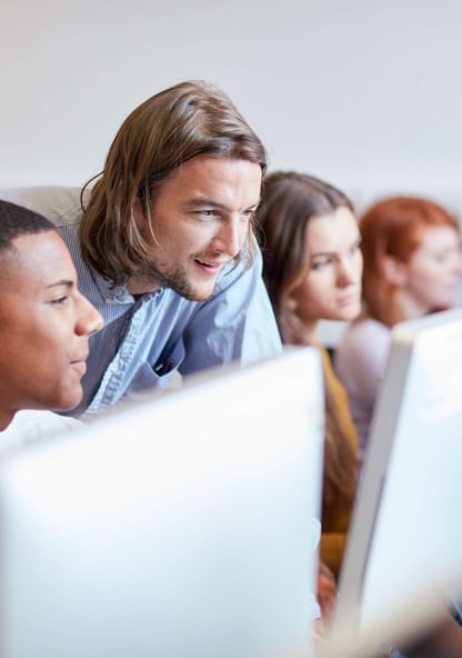 a professor stops to help students working on their computers