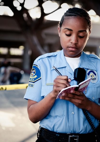 an officer stands outside of the police tape and writes notes in a notepad