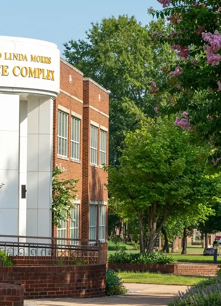 Exterior of the Ray and Linda Morris Science Complex with columns, landscaping, and a campus walkway on a sunny day.