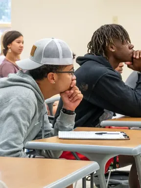 College students attentively listening during a lecture, seated at desks in a classroom.
