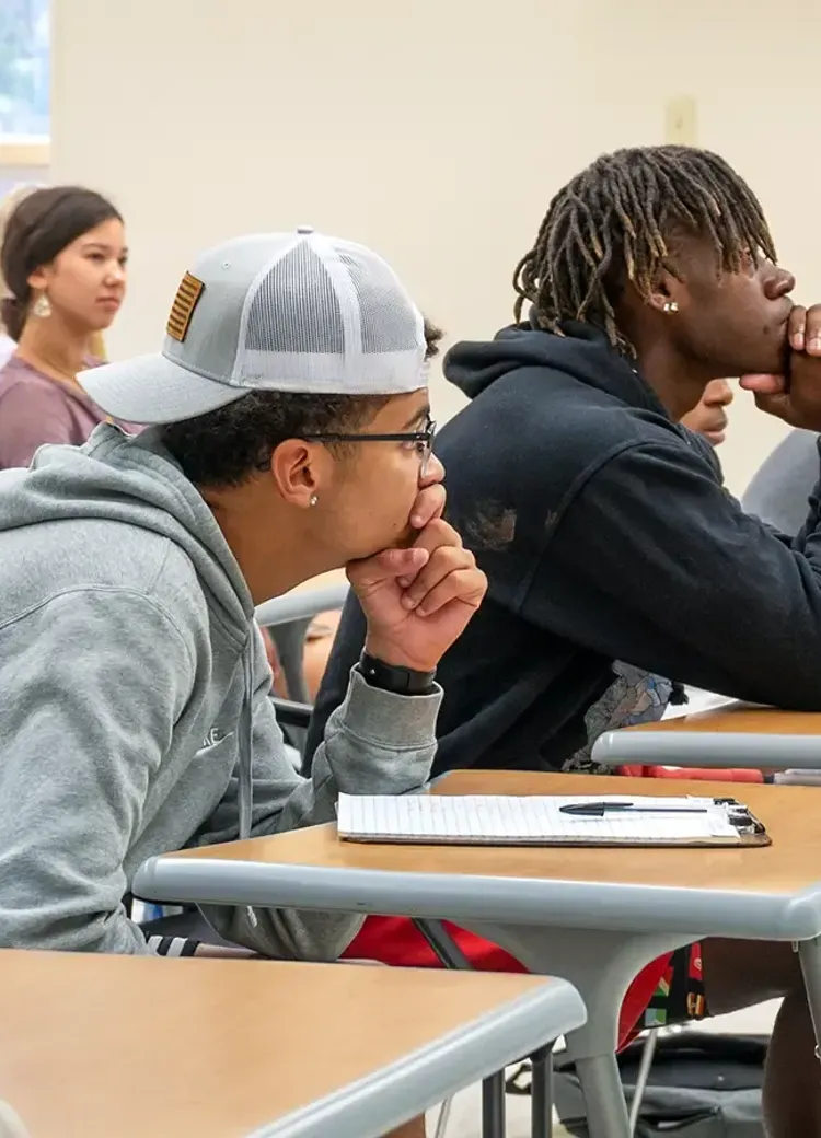 College students attentively listening during a lecture, seated at desks in a classroom.