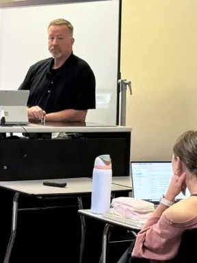 Two law enforcement professionals presenting to a student in a college classroom.
