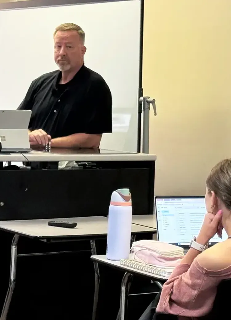 Two law enforcement professionals presenting to a student in a college classroom.