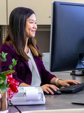 A college student working at a desktop computer at an office desk.