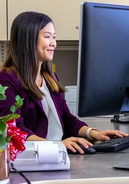 A college student working at a desktop computer at an office desk.