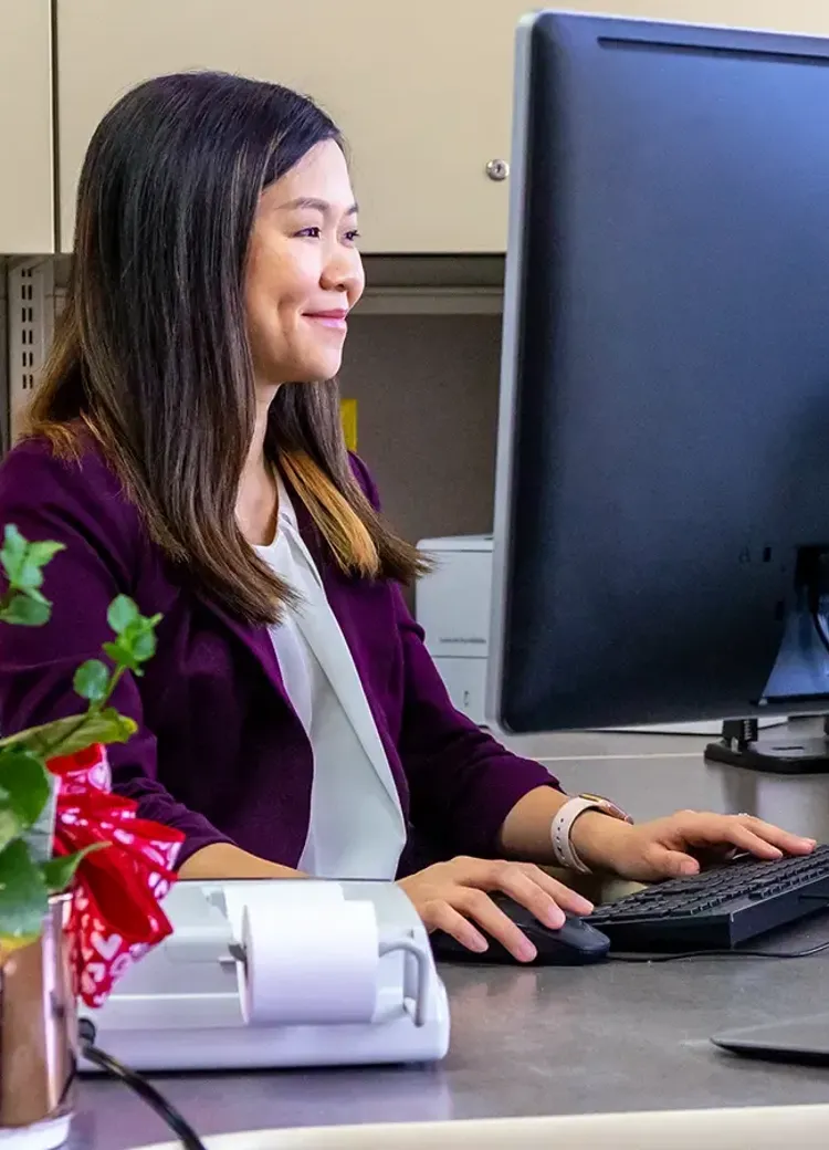 A college student working at a desktop computer at an office desk.
