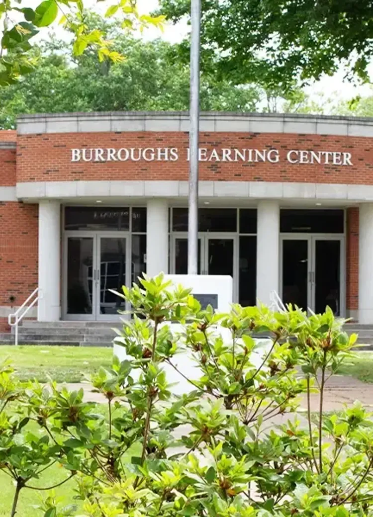 The Burroughs Learning Center at Bethel University, a one-story brick building with a columned entrance, framed by trees and flowering shrubs.