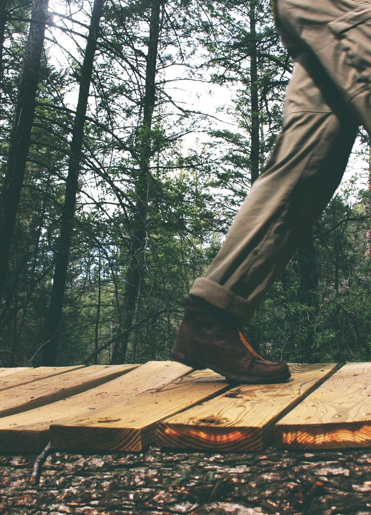 man in boots walks across a wooden bridge