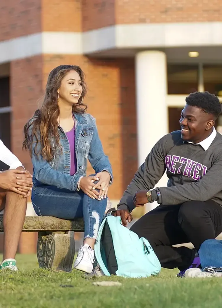 Four Bethel students sit and talk together outside the library.