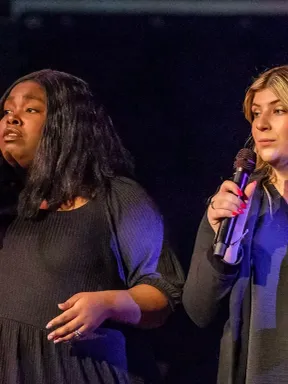 Two students sing into microphones during a performance on stage.